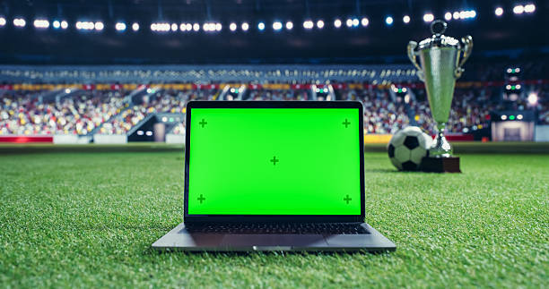 istock Laptop Computer with a Green Screen Template Standing on a Soccer Pitch with a Trophy and Soccer Ball in the Background. Mock Up Display Suitable for Adding Sports-Themed Digital Content 2205704913