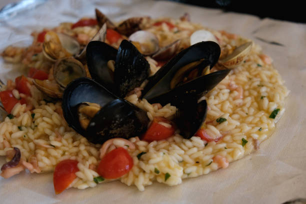 Shot of a delicious plate of creamy seafood risotto with fresh mussels, clams, cherry tomatoes, and herbs.\nConcepts: seafood risotto, Italian cuisine, gourmet food, Mediterranean dish, fine dining, mussels and clams, creamy rice, restaurant meal