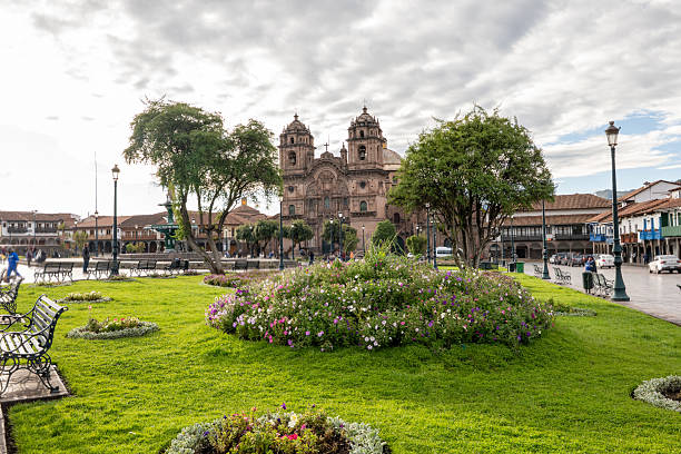Lush green plaza with vibrant flowers surrounds Cusco Cathedral. Historic architecture and scenic benches create a peaceful urban retreat. Ideal for tourism and travel content.