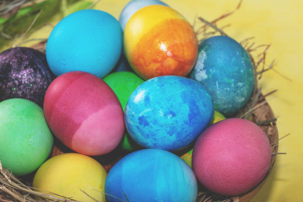 Colorful easter eggs in a basket on a yellow wooden table