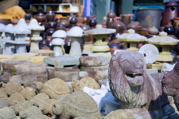 Gwangyang, South Korea - October 3rd, 2021: A collection of handcrafted stone sculptures, including turtles, lanterns, and a lion carving, displayed alongside traditional Korean earthenware pots at a roadside market near the Seomjingang Bike Path.
