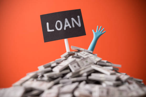istock Pop out hand from heap US dollar banknotes and LOAN label red wall background. 2205719495