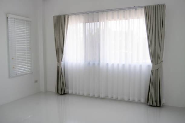 Sunlight streams through sheer curtains, creating a striped pattern on the interior. A potted plant sits on a windowsill, adding a touch of nature to the inviting space.