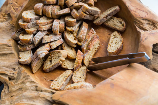 Slices of brown bread in a wooden bowl with iron tongs