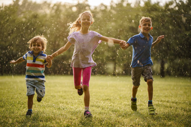 istock Children holding hands while running on a rainy sunny day in the park 2205724966