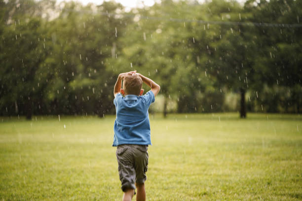 Rear view of little boy running during rainy summer day in public park