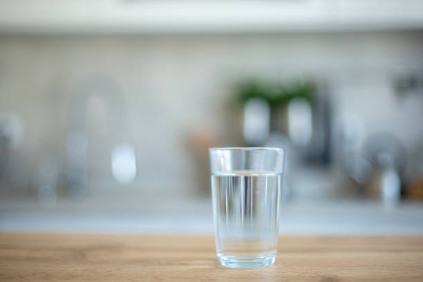 Close-up, selective focus on glass of clean water on wooden table with domestic kitchen in background as copy space.