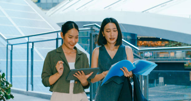 istock Two young Asian businesswomen digital tablet discuss renewable energy solutions beside staircase equipped with solar panels while walking in urban environment. Sustainable business outdoor. 2205728596