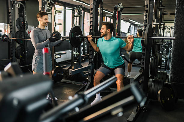 istock Fit man does barbell squats with the help of his personal trainer. 2205730687