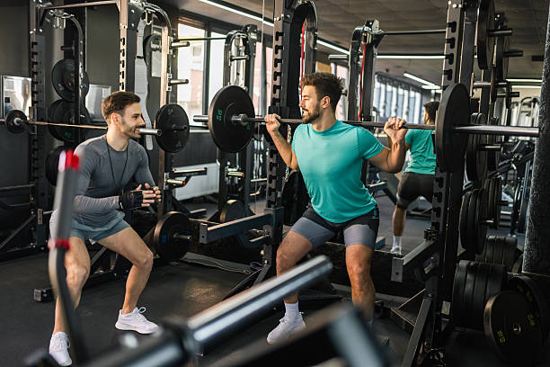istock Fit man does barbell squats with the help of his personal trainer. 2205730702