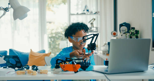 istock Young African-American boy explores robotics and engineering at home, demonstrating enthusiasm and focus during an online educational session. STEM Education robotics courses online. 2205736363