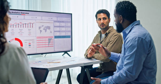 istock Group of business professionals meeting reviewing global data analytics presented on a large screen, discussing strategy and growth at the office. Finance meeting concept. 2205738328