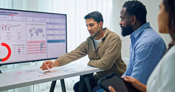 istock Group of business professionals meeting reviewing global data analytics presented on a large screen, discussing strategy and growth at the office. Finance meeting concept. 2205738340