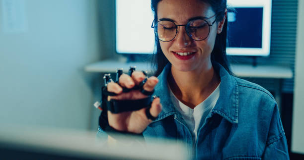 istock Young female engineer working late gestures towards robotic arm in tech lab at night. Machine learning, computer manufacturing, innovation and creativity. AI and Robotics Development. 2205739539