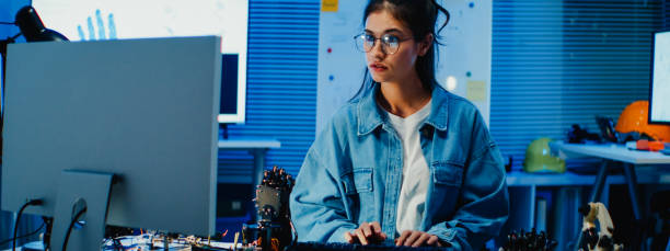 istock Young female engineer working late on a robotic arm prototype in tech lab at night. Machine learning, computer-aided manufacturing, innovation and creativity. AI and Robotics Development. 2205739590