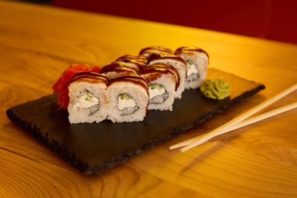 istock Fresh sushi rolls filled with cream and vegetables are stylishly presented on a black stone plate. Vibrant wasabi and pickled ginger accompany the dish in a cozy dining setting 2205742404