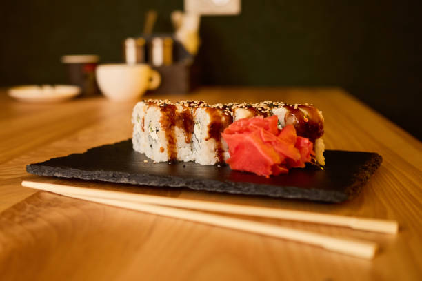 A beautifully presented sushi roll sits on a black slate plate, garnished with pickled ginger. The inviting atmosphere of the restaurant enhances the dining experience during dinner