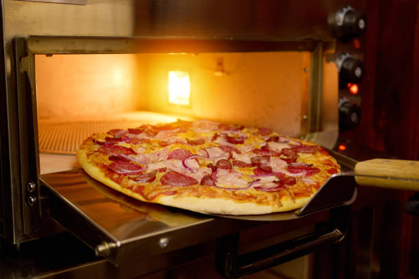 istock A freshly baked pizza with pepperoni, ham, and onions is being carefully pulled from the oven in a warm, inviting kitchen environment during the evening 2205742497