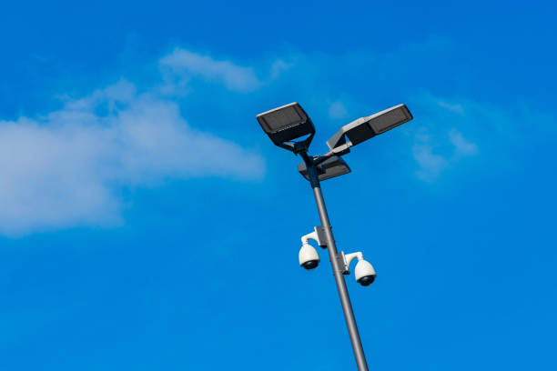 Two solar-powered street lights and surveillance cameras stand tall against a bright blue sky, showcasing modern urban infrastructure. The scene emphasizes safety and efficiency in city design.