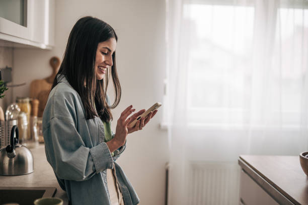 istock Young woman using smartphone and smiling in kitchen 2205746285