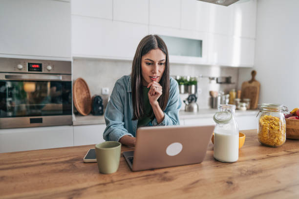 istock Focused young woman working remotely from home kitchen using laptop 2205746608
