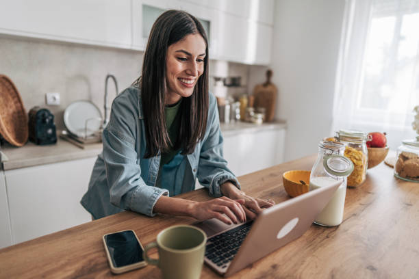 istock Young woman working remotely from home using laptop in kitchen 2205746694