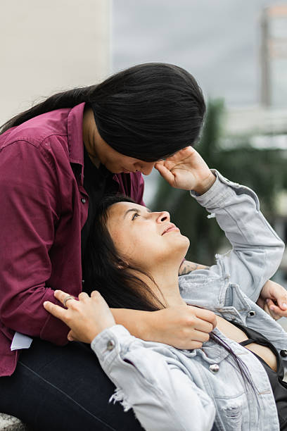 young latina lesbian woman lying on her partner's lap looking up at her while caressing his face