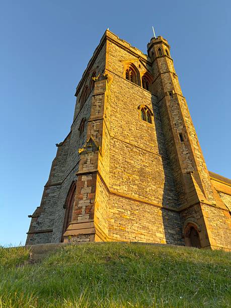 istock A striking historic stone tower with Gothic-style windows, bathed in warm golden sunlight against a clear blue sky. 2205747552