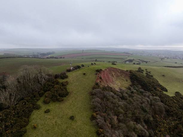 istock Aerial image of rolling hills featuring a red soil exposedby ancient mine collapse, contrasting against green fields, with distant farmland under a cloudy sky. 2205747556