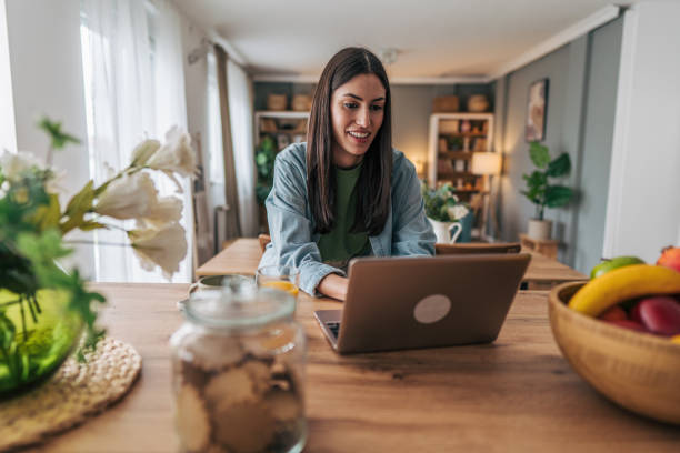 istock Young woman working from home on laptop in kitchen 2205749266