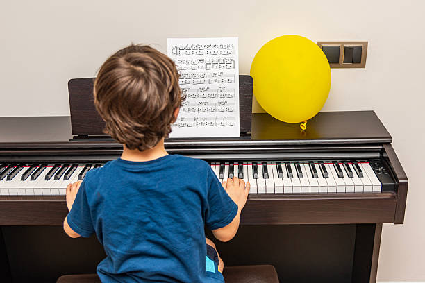 A young boy having fun practicing piano and yellow balloon