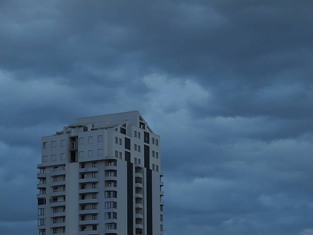 A contemporary residential highrise building stands against a backdrop of dramatic storm clouds, creating a moody and atmospheric cityscape. Captured in natural lighting, the image highlights urban architecture and the contrast between structure and sky.