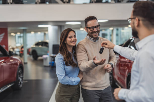 Happy couple receiving new car keys from salesman in dealership Happy couple smiling and receiving new car keys from a car salesman in a dealership, they just bought their new car and are excited to drive it home car finance stock pictures, royalty-free photos & images
