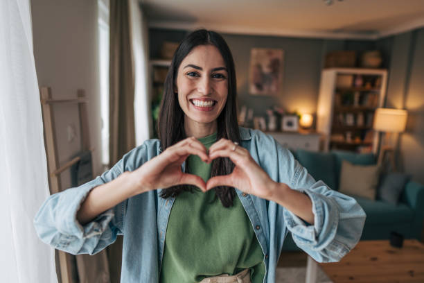 istock Young woman making heart shape with hands at home 2205765767