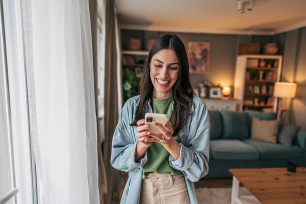 istock Young woman using mobile phone, browsing internet and smiling at home 2205765902