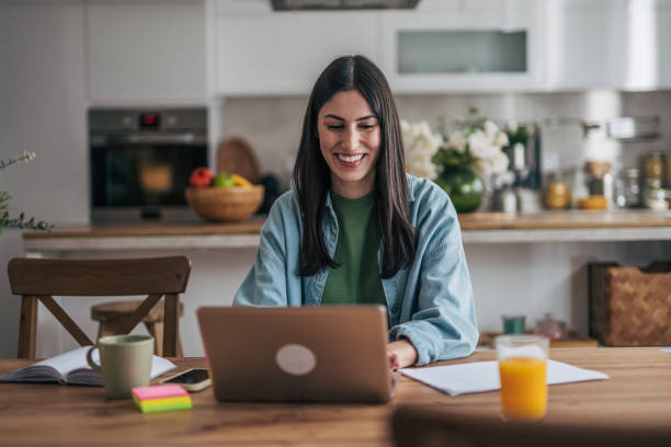 istock Young woman working from home on laptop in kitchen 2205765971