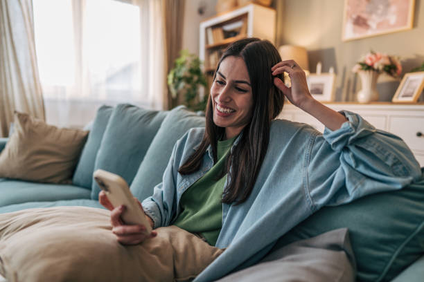 istock Young woman relaxing on sofa using smartphone and touching hair 2205767153