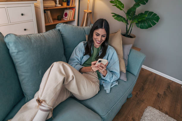 istock Young woman relaxing on sofa using smartphone at home 2205767515