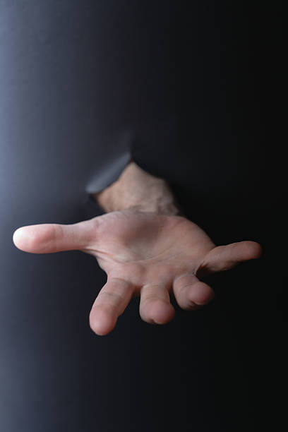 istock photo Close-up of an open hand reaching out through dark surface symbolizing help, human connection, touch, support and the concept of asking or offering assistance 2205769456