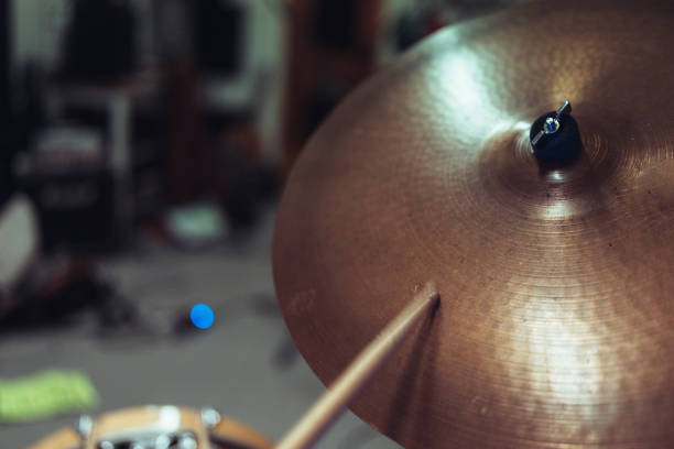 Close-up of a drumstick aimed at a cymbal in a rehearsal studio. The blurred background adds depth, emphasizing the action and energy of drumming.