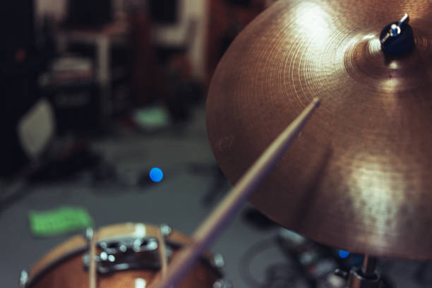 Close-up of a drumstick aimed at a cymbal in a rehearsal studio. The blurred background adds depth, emphasizing the action and energy of drumming.