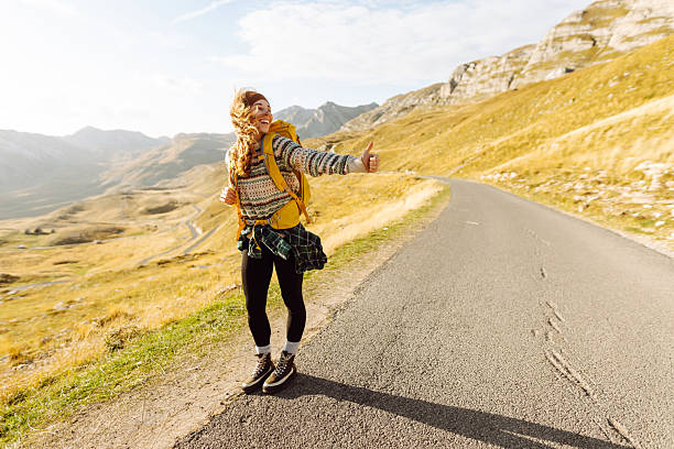 Backpacking woman on a deserted road thumbs up. Hitchhiking woman traveler try to stop car