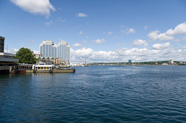 A view of Halifax from the harbour on a sunny summer morning, with the Angus L. Macdonald Bridge visible in the background, stretching across the calm water.