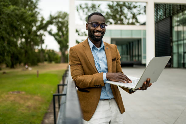 istock Happy black businessman using laptop outdoors and looking at camera. 2205775661