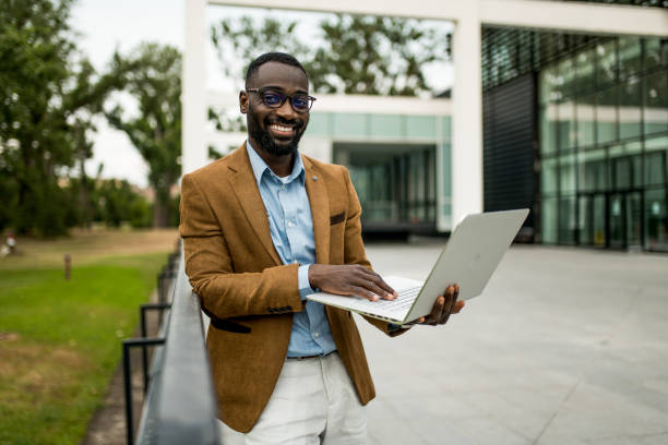 istock Happy black businessman using laptop outdoors and looking at camera. 2205776222