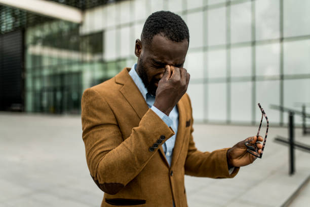 Tired black businessman having eyesight problems outdoors.