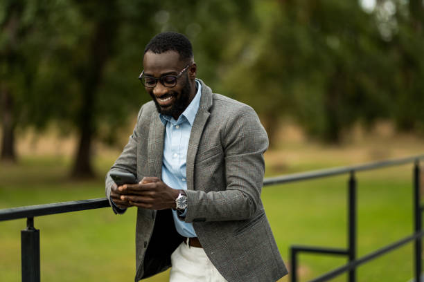 Happy young African American male entrepreneur using mobile phone outdoors.