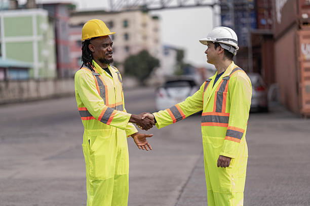 istock Two industrial workers in high-visibility safety gear shake hands at a shipping container yard, symbolizing teamwork, partnership, and successful collaboration in logistics and supply chain management. 2205779241