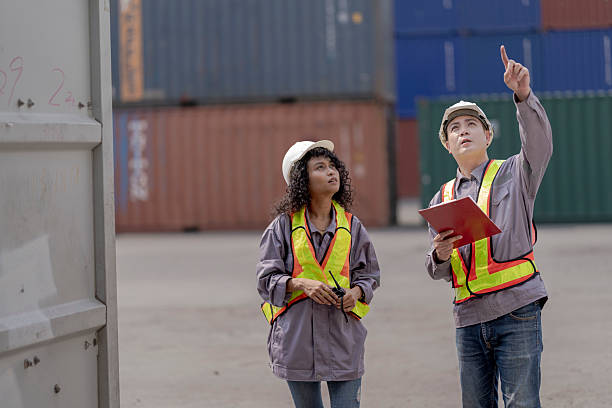 istock Two logistics workers asian man and woman discuss operations at a busy shipping container yard. One is holding a tablet while pointing towards the cargo stacks. 2205779637