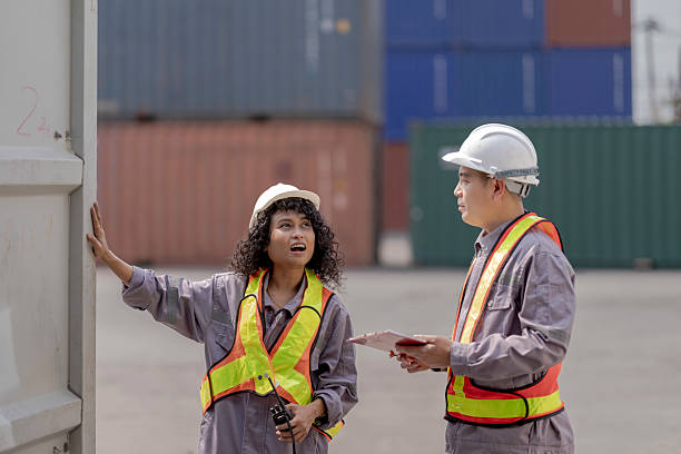 istock Two logistics workers asian man and woman discuss operations at a busy shipping container yard. One is holding a tablet while pointing towards the cargo stacks. 2205779640